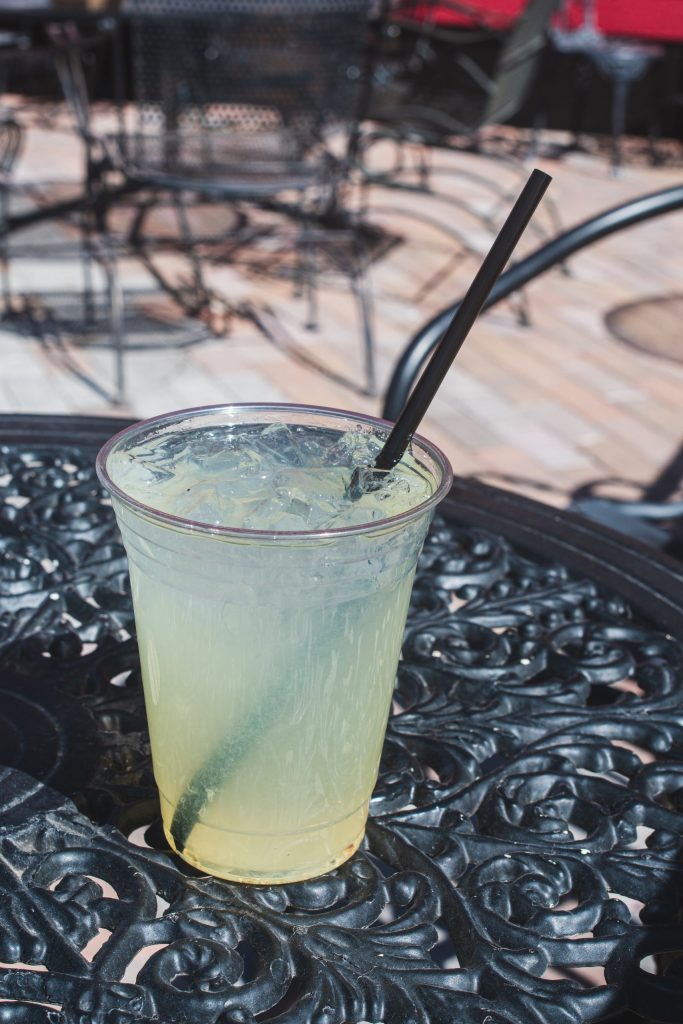 Plastic cup of lemonade with straw on ornate metal table outdoors.