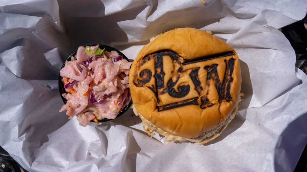 Burger bun with 'PW' design next to coleslaw in a paper tray.