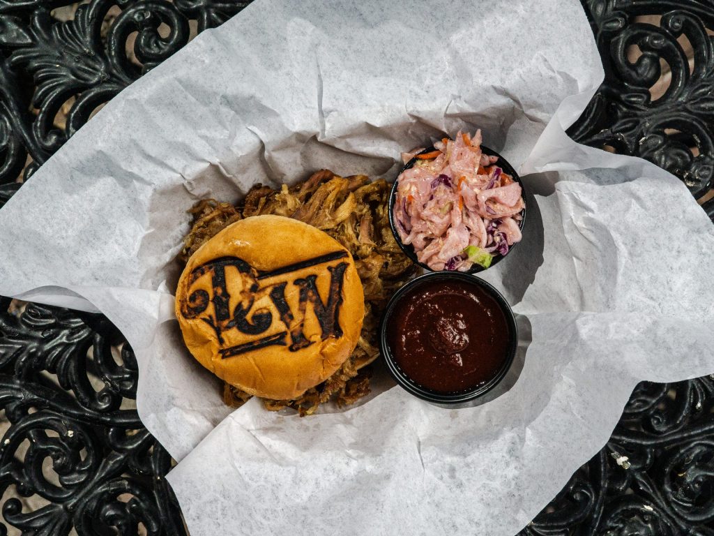 Pulled pork sandwich with BBQ sauce and coleslaw on white paper.