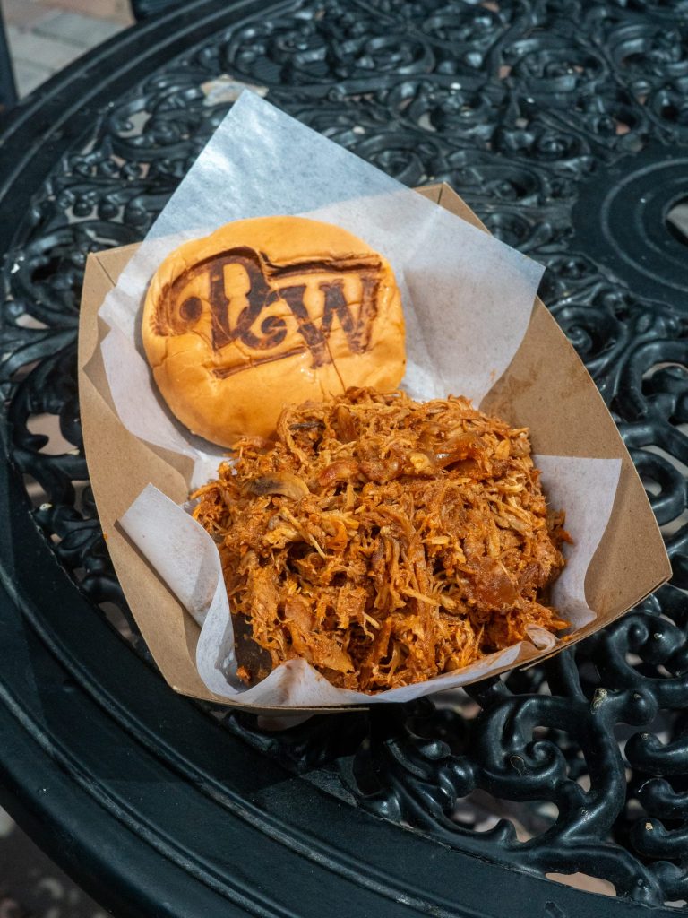 Pulled pork sandwich with branded bun on a black metal table.