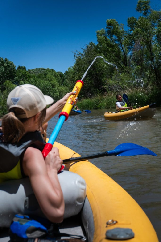 People kayaking on a river, person spraying water from a toy.